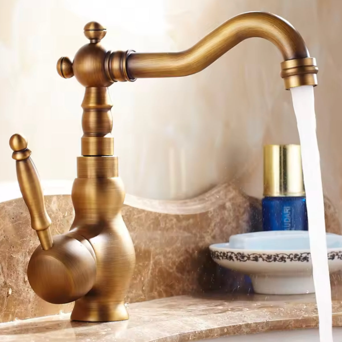 Mitigeur de lavabo ORVAN en laiton vieilli sur un plan en marbre, eau en écoulement