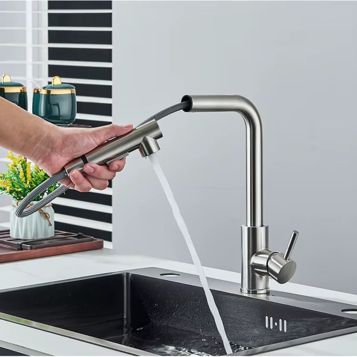 Douchette extractible du robinet de cuisine ASVIK gris tenue à la main au-dessus de l'évier